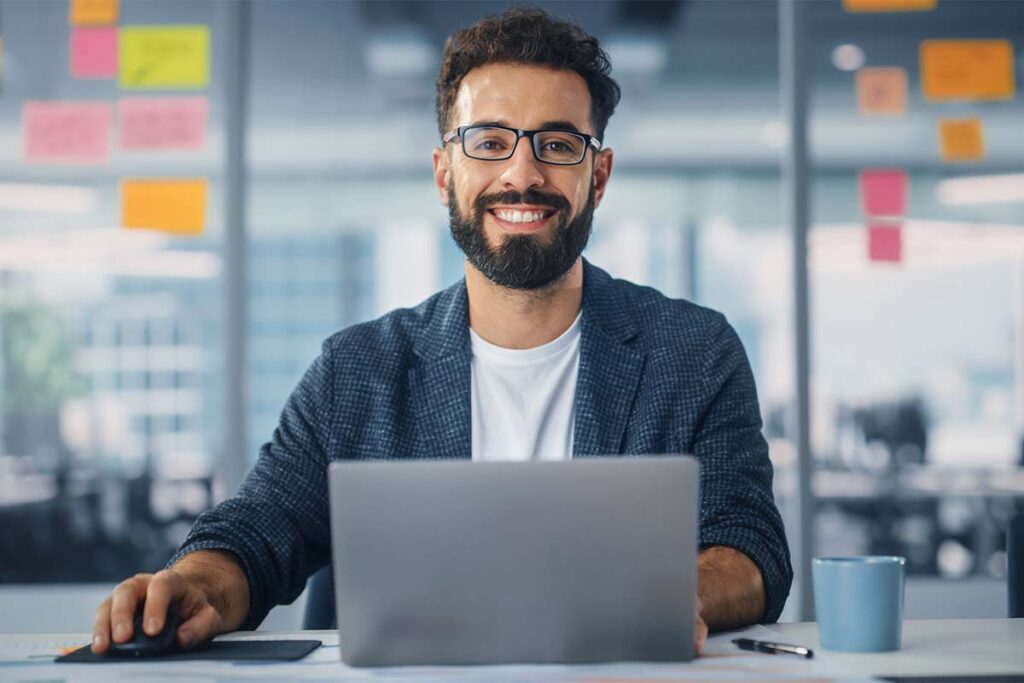 Gentle man working on laptop in an office with a glass wall with notes.